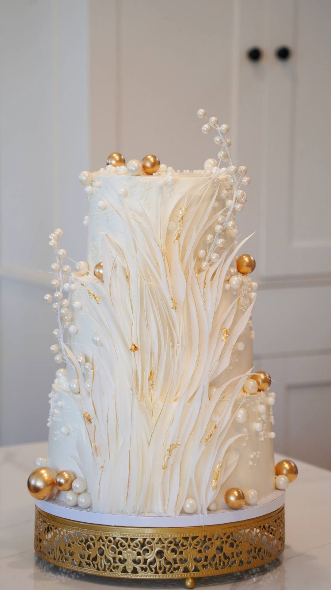 Three-tier white wedding cake with sugar feathers, pearls and gold