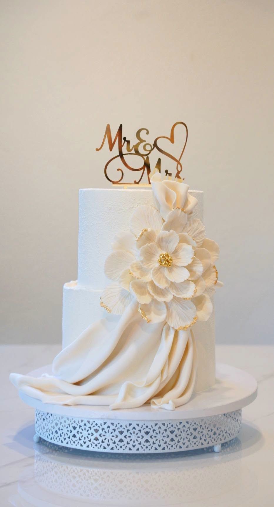 Two-tier white wedding cake with sugar flower and fondant drape